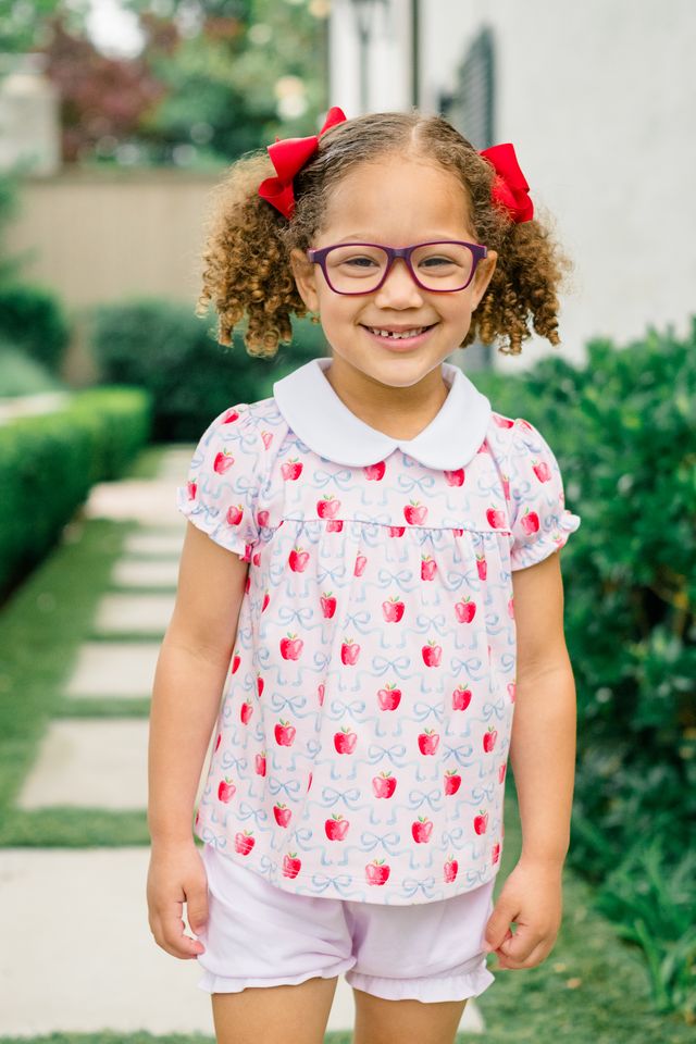 Dress your little one in the enchanting Apple Blossoms Bloomer Set by The Proper Peony. This delightful ensemble features charming apple and bow prints, complemented by a soft white Peter Pan collar. Crafted from luxurious Pima cotton, it offers unmatched comfort—perfect for those memorable first school days!