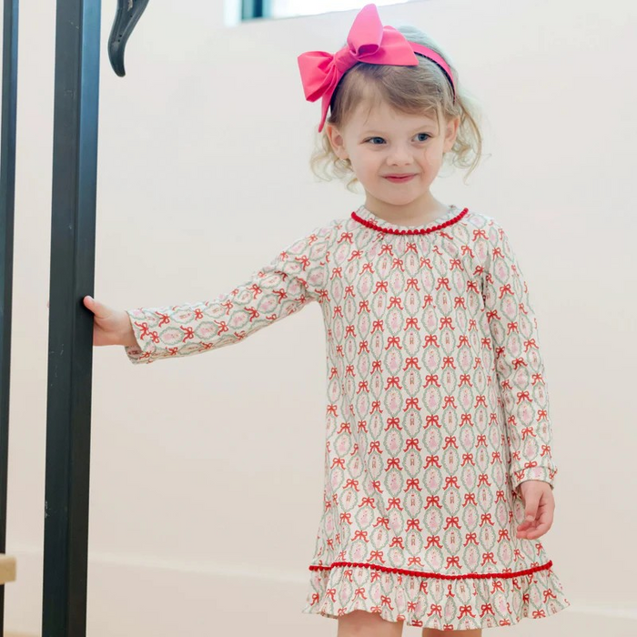 Dress your little one in enchanting elegance with the Carlin Girls' Dress featuring a charming Nutcracker Ballet print from Lila &amp; Hayes. Made from soft, breathable long-sleeve pima cotton, it ensures comfort all day. The flutter ruffle hem and delicate pom pom trim add playful details, while the button closure at the back makes dressing effortless. Perfectly pairs with the matching Doll Dress for an adorable coordinated look that captures the magic of the season.