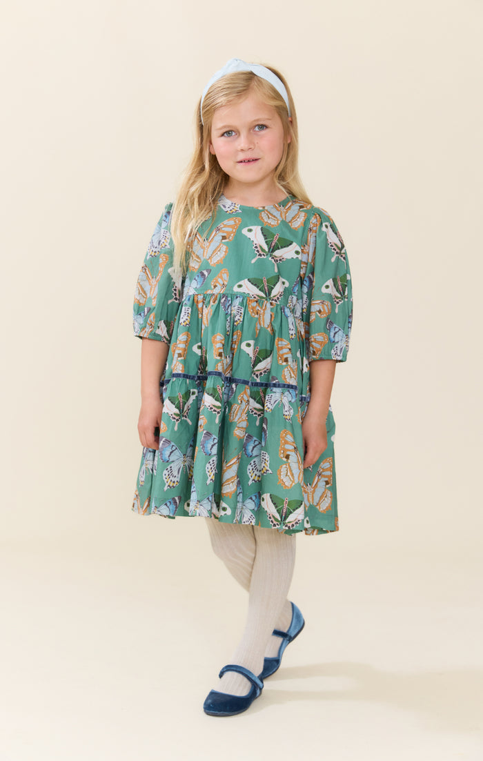 Pink Chicken’s Girls Maribelle Dress in Green Butterflies brings playful elegance to every twirl. The delicate butterfly print and navy velour ribbon trim create a charming look that delights and inspires confidence in every step. Perfect for joyful moments and unforgettable memories!