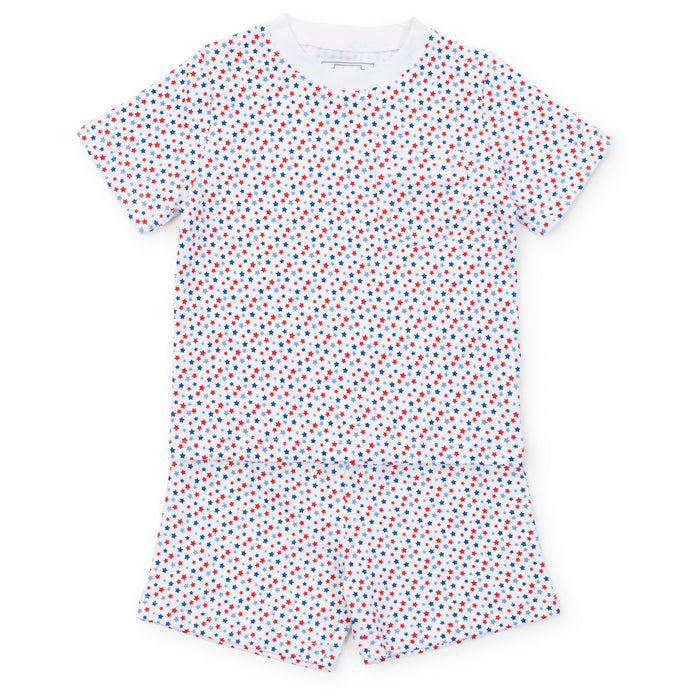Experience the ultimate comfort and style with our Star Spangled Charles Pajama Short Set from Lila &amp; Hayes. Made from soft cotton material, this set includes a short sleeve shirt and coordinating shorts, adorned with fun red and blue stars. Perfect for a cozy night's sleep or lounging around in style.