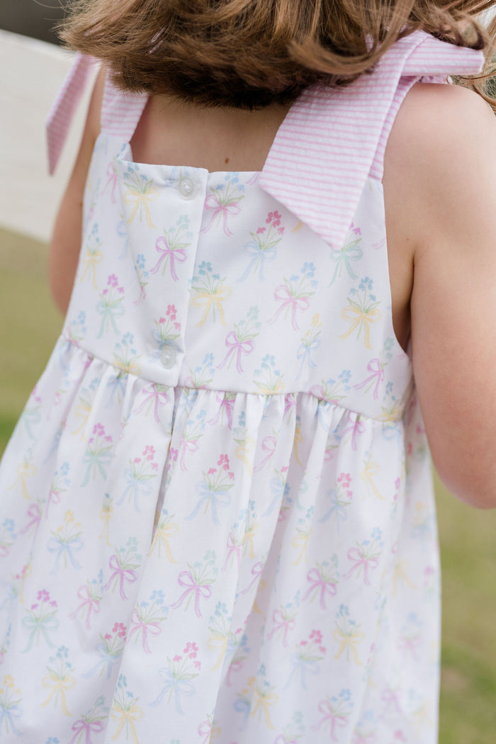 Indulge in the beauty of nature with Thea Flower Bouquet Dress from James &amp; Lottie! Adorned with floral bouquets and cute bows, this dress exudes a sense of elegance. The pink and white seersucker ties on the shoulders add a charming touch. Perfect for any occasion, this dress will make you feel like a blooming flower!